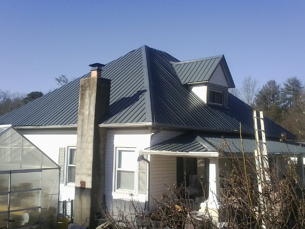 Dark blue standing seam metal roof on a white farmhouse with dormer — Slate & Tile Roof Repair by Roofing Brothers in Gary