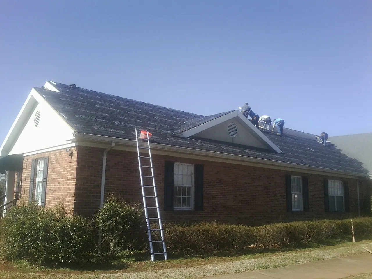 Crew tearing shingles off a brick ranch roof with a ladder set — Metal Roof Repair work by our crew in Gary
