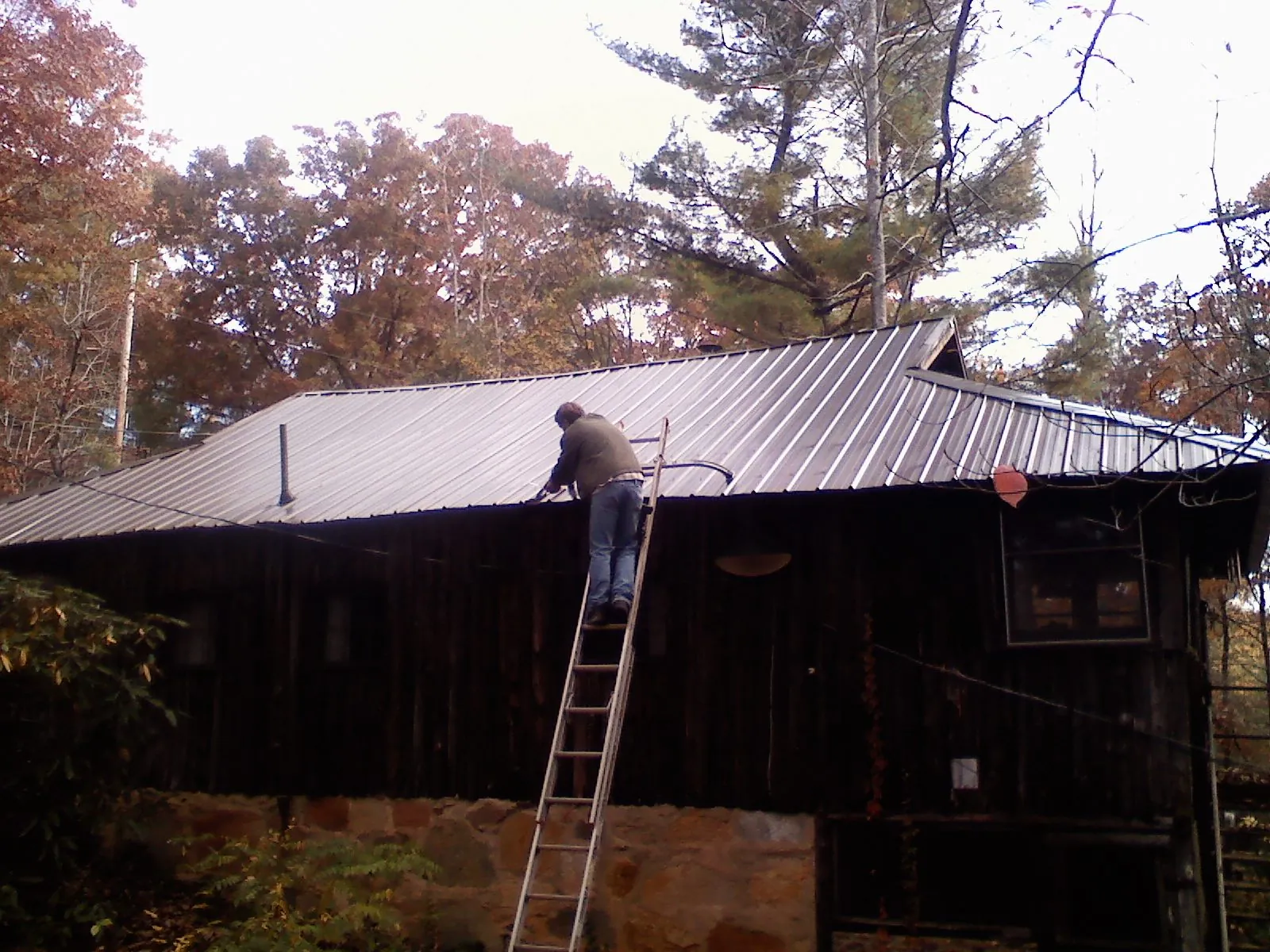 Roofer on a ladder working along the edge of a cabin metal roof in Gary